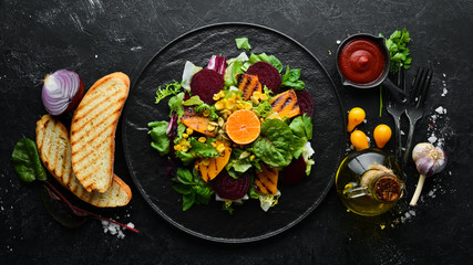 Obraz na płótnie Canvas Salad: beetroot, pumpkin, corn and lettuce in a black plate on a black background. Top view. Free space for your text.