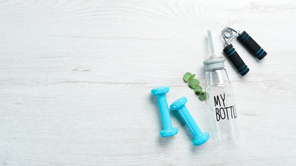 Naklejka premium Fitness dumbbells, expander and water bottle. On a white wooden background. Flat lay.