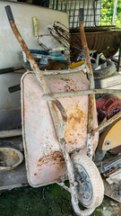 Fototapeta premium An old rusty 3-wheeled wheelbarrow leaning back at the storage place.