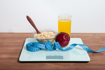 The concept of healthy diet, fitness and weight loss. Scales, measure tape, oatmeal, apple, a glass of juice on the table.