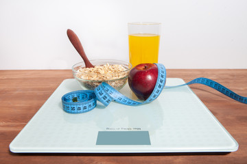 The concept of healthy diet, fitness and weight loss. Scales, measure tape, oatmeal, apple, a glass of juice on the table.
