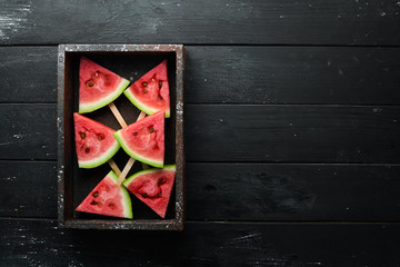 Watermelon popsicle on black background. Watermelon slices on sticks. Top view. Free copy space.