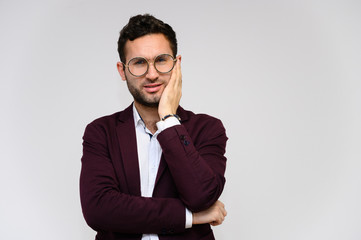 Men's fashion concept. Portrait of a handsome male model in glasses shows hands wearing a dark jacket, posing on a gray background. Black hair. Close Studio Shot