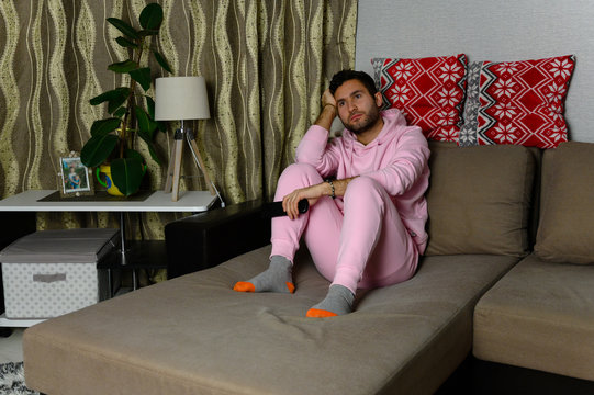 Young television addict man sitting on sofa at home and watching TV using remote control, looking bored and tired, pumping someone else's comedy comedy movie or live music at night