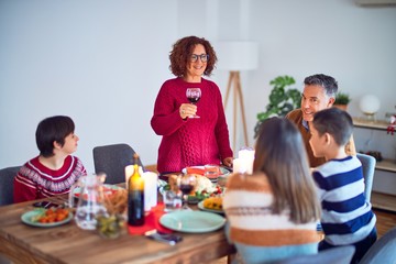 Beautiful family smiling happy and confident. One of them standing holding cup of wine speaking speech celebrating thanksgiving day at home