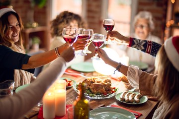Beautiful group of women smiling happy and confident. Eating roasted turkey and toasting with cup of wine celebrating christmas at home