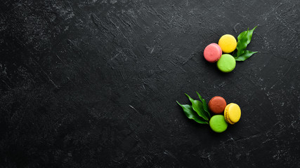 Macaroons colored cakes. On a black stone background. Top view. Free space for your text.