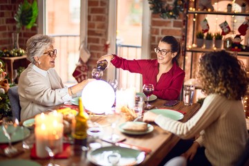 Beautiful group of women smiling happy and confident. Eating roasted turkey and serving wine on cup celebrating christmas at home