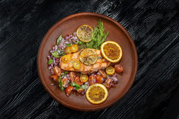 Grilled salmon and vegetables. Laid on a beautiful clay plate, sprinkled with onions, dill and tomatoes.