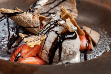 Plate with ice cream and waffles, poured with chocolate topping and decorated with strawberries.