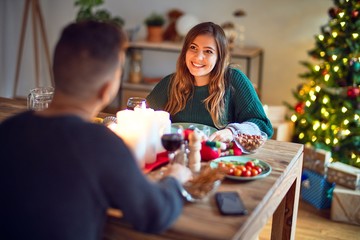 Young beautiful couple smiling happy and confident. Eating food celebrating christmas at home