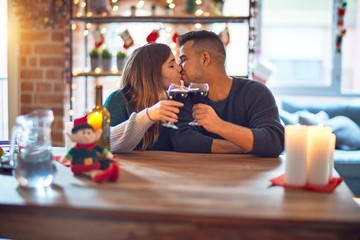 Young beautiful couple smiling happy and confident. Toasting with cup of wine and kissing celebrating christmas at home