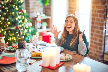 Young beautiful woman sitting eating food around christmas tree at home celebrating mad and crazy...