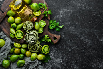 Raw green pasta with tomatoes, oil and parsley on a black stone background. Italian traditional cuisine. Fresh vegetables. Top view. Free space for your text.