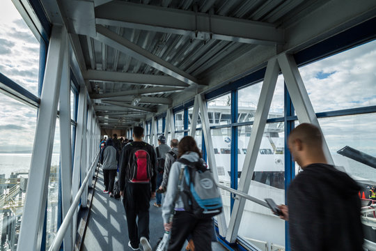 A passenger ferry terminal gangway with travellers walking with their luggage towards a ferry waiting to depart.