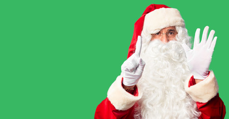 Middle age handsome man wearing Santa Claus costume and beard standing showing and pointing up with fingers number six while smiling confident and happy.