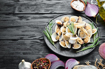 Boiled clams with spices in a plate. Seafood on black background. Top view. Free copy space.