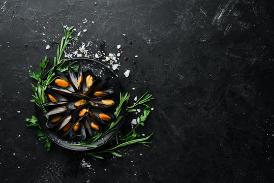 Mussels with spices and rosemary. Seafood on black background. Top view. Free copy space.