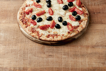 Pizza with mozzarella cheese, cherry tomatoes, black olives and oregano. Home made food. Concept for a tasty and hearty meal. Rustic wooden background. Copy space. 