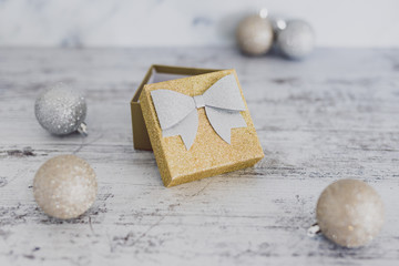 Christmas gift box with baubles around it wth gold and silver colors on wooden desk