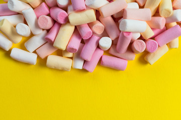 Multi-colored little marshmallows on a bright yellow background. Copy space.