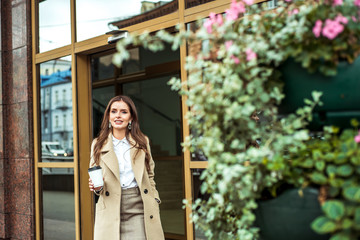 Bright warm autumn day in the metropolis. Street Veta on the flowerbed.Portrait of beautiful brunette girl walking down the street. Keeping takeaway drink in one hand Urban city scene.Outdoors