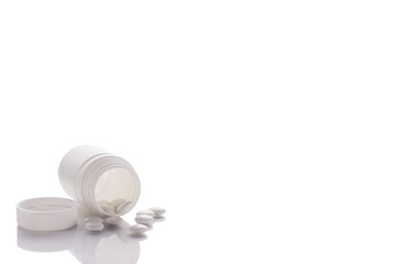 A jar with poured tablets lies on a mirror surface on a white background on the left side.