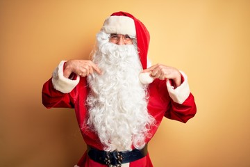 Middle age handsome man wearing Santa costume standing over isolated yellow background looking...