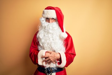 Middle age handsome man wearing Santa costume standing over isolated yellow background skeptic and nervous, disapproving expression on face with crossed arms. Negative person.