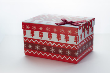 Christmas box with red gifts on white isolated background with the image of Christmas trees close-up angled. There is a bow in the corner