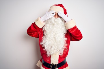 Middle age handsome man wearing Santa costume standing over isolated white background covering eyes with hands smiling cheerful and funny. Blind concept.