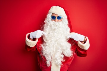 Middle age man wearing Santa Claus costume and sunglasses over isolated red background looking confident with smile on face, pointing oneself with fingers proud and happy.