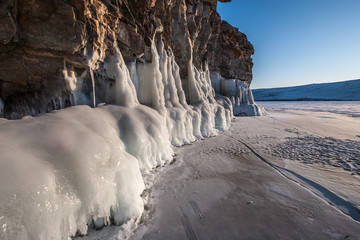 A thick layer of ice on a rock lit by the sun. The lake is covered with ice and snow.
