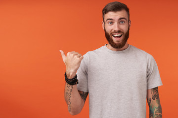 Happy pretty bearded tattooed man with trendy haircut looking at camera with wide smile and...