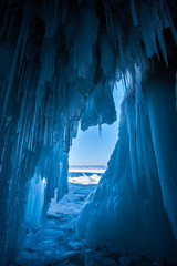 View from an ice cave with huge blue icicles on Lake Baikal. Crystal stalactites on the ceiling. A lot of broken ice outside the cave.