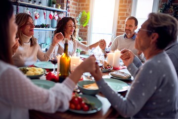 Family and friends dining at home celebrating christmas eve with traditional food and decoration, praying and blessing the table