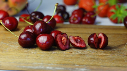 Leckere und saftige Kirschen, ganz und aufgeschnitten, auf Holz mit Erdbeeren im Hintergrund
