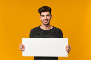 Young man over isolated background holding an empty white placard for insert a concept