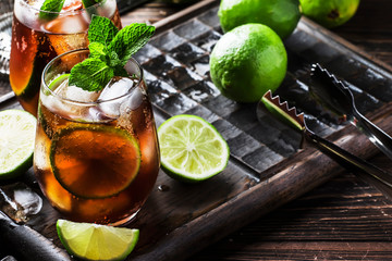 Cuba libre alcohol cocktail with golden rum, lemon juice, cola, lime and ice, dark bar counter background, bar tools, place for text