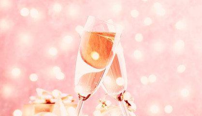 Two champagne glasses and christmas decoration over pink golden bokeh background. Happy New Year Celebration. Selective focus and small depth of field