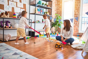 Beautiful teacher and toddlers playing tennis using racket around lots of toys at kindergarten
