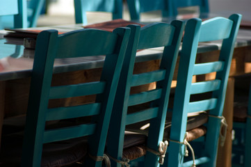 Empty taverna tables and seating at a restaurant in a square on the island of Folegandros. Close up detail emphasises the simplicity and beauty of the simple design of these traditional chairs.