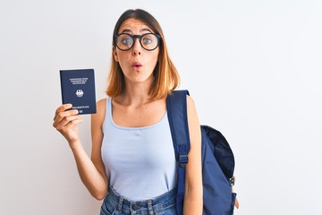 Fototapeta premium Beautiful redhead student woman wearing backpack and holding passport of germany scared in shock with a surprise face, afraid and excited with fear expression