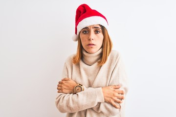 Beautiful redhead woman wearing christmas hat over isolated background shaking and freezing for winter cold with sad and shock expression on face