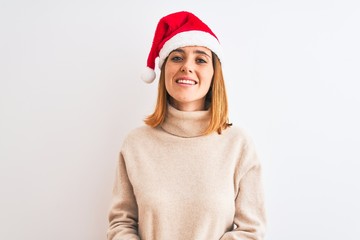 Fototapeta premium Beautiful redhead woman wearing christmas hat over isolated background with hands together and crossed fingers smiling relaxed and cheerful. Success and optimistic