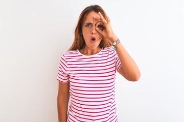 Young redhead woman wearing striped casual t-shirt stading over white isolated background doing ok gesture shocked with surprised face, eye looking through fingers. Unbelieving expression.