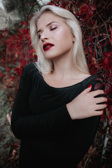 Incredible, amazing, girl in a dress of magic. Fantastic autumn background. Art photography. Blonde in a black dress in the fall. makeup with burgundy lipstick