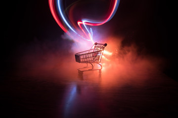 Empty shopping trolley on dark toned foggy background with some copy space. Financial crisis...