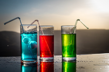 Cooling summer drink concept. Cocktail glasses splashing on sunset. Close up wet glass of cold...