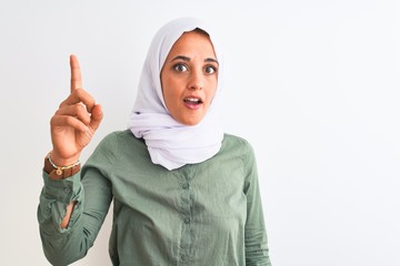 Young beautiful Arab woman wearing traditional Muslim hijab over isolated background pointing finger up with successful idea. Exited and happy. Number one.